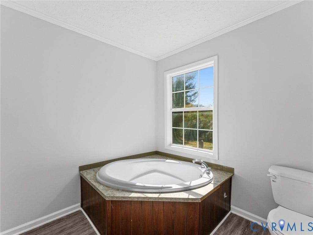 1625 Cedar Lane, Powhatan, VA 23139 Corner soaking tub featuring a stone-finish deck, wood-toned cabinetry, polished chrome faucet, and window with natural light
