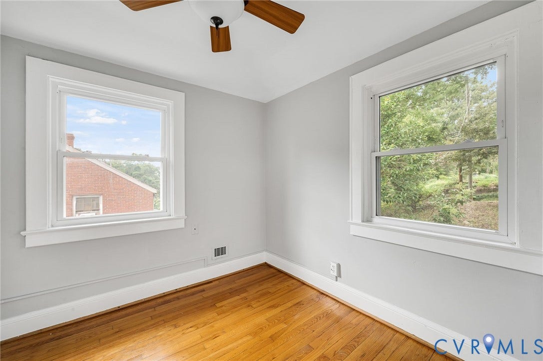 602 N 39th Street, Chimborazo, Richmond, VA 23223 Neutral-toned interior room featuring wood-finish flooring, two double-hung windows with white casing, and a ceiling-mounted fan with wooden blades