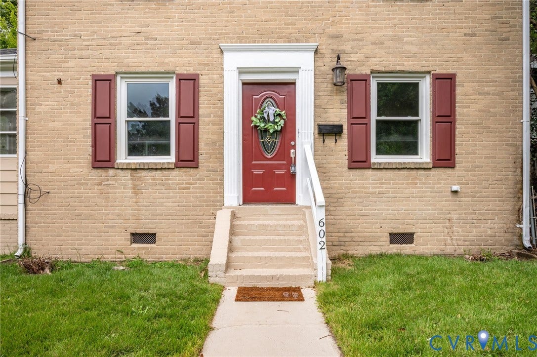 602 N 39th Street, Chimborazo, Richmond, VA 23223 Exterior facade featuring tan brick masonry, red shutters, a central entrance with a white fluted door surround, an oval glass-paneled door, and concrete steps with a white handrail