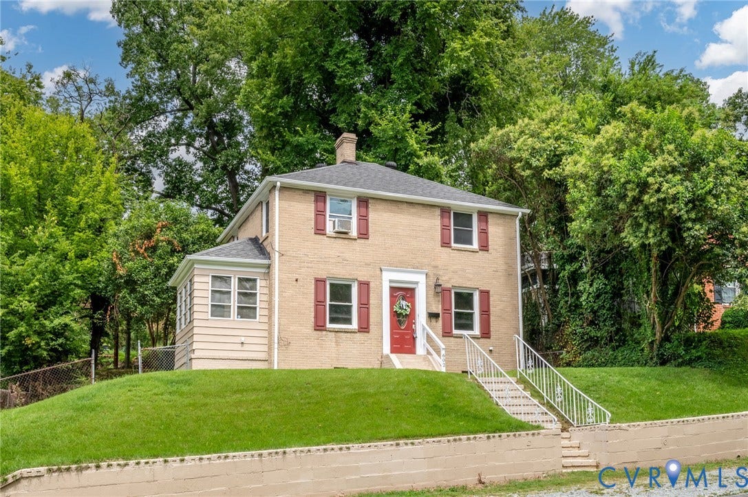 602 N 39th Street, Chimborazo, Richmond, VA 23223 Two-story brick exterior featuring a hipped roof, contrasting window shutters, a front entry with metal railing, and a stone retaining wall