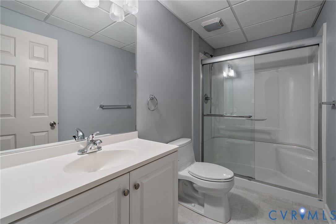 10862 Walton Lake Road, Dick Woods Subdivision, Disputanta, VA 23842 Bathroom featuring a white vanity with an integrated sink, a large wall-mounted mirror, a two-piece toilet, and a glass-enclosed shower with a built-in bench