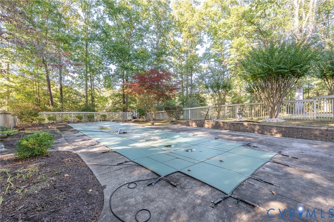 10862 Walton Lake Road, Dick Woods Subdivision, Disputanta, VA 23842 In-ground pool with fitted safety cover, expansive concrete pool deck, stone retaining wall, and wood-slat perimeter fencing surrounded by mature trees