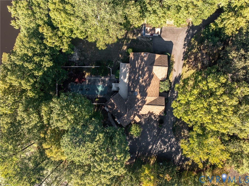 10862 Walton Lake Road, Dick Woods Subdivision, Disputanta, VA 23842 Aerial perspective of a wooded lot featuring a multi-pitched roof, an asphalt driveway, and a paved patio area
