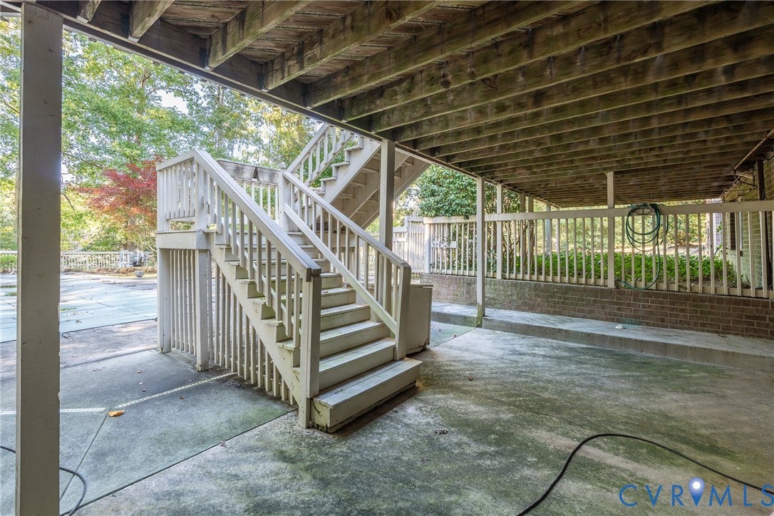 10862 Walton Lake Road, Dick Woods Subdivision, Disputanta, VA 23842 Covered patio area with a concrete floor, structural wood-beam ceiling, brick knee wall, and exterior wooden staircase with balustrades