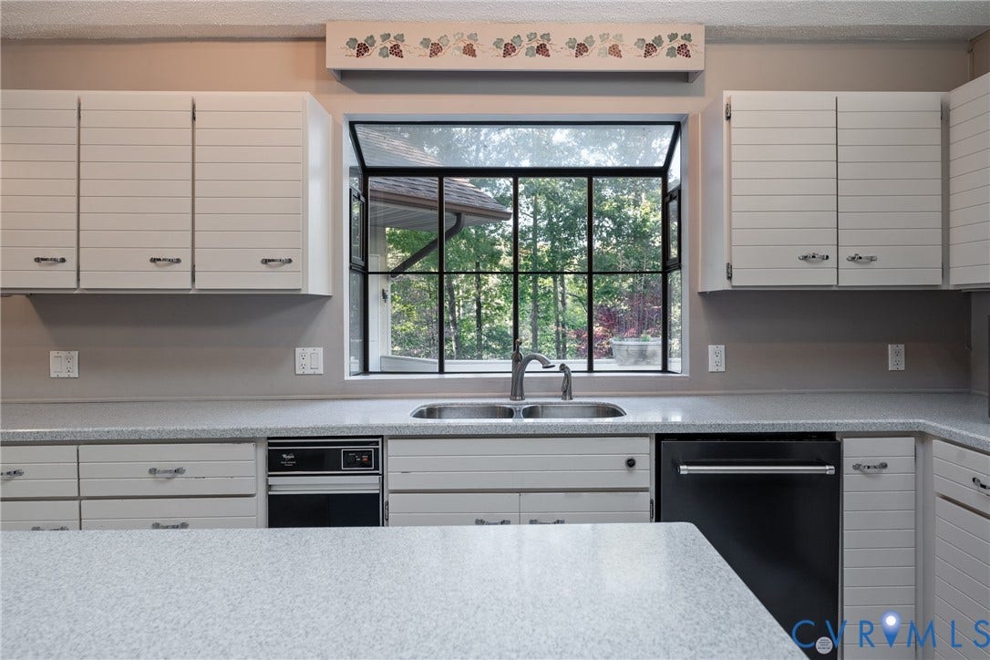 10862 Walton Lake Road, Dick Woods Subdivision, Disputanta, VA 23842 Kitchen featuring horizontal-paneled cabinetry, solid-surface countertops, dual-basin stainless steel sink with arching faucet, and large-format garden window