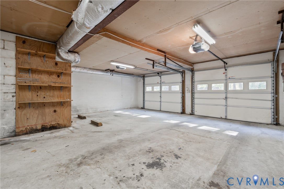 10862 Walton Lake Road, Dick Woods Subdivision, Disputanta, VA 23842 Two-car garage featuring segmented overhead doors with windows, exposed ceiling joists, concrete flooring, and built-in wood shelving