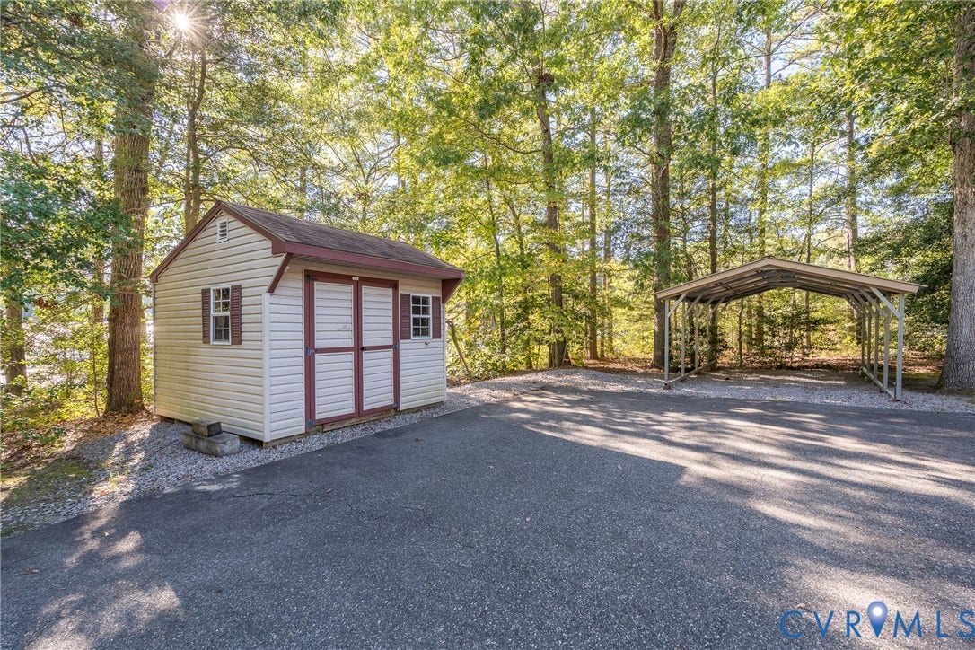 10862 Walton Lake Road, Dick Woods Subdivision, Disputanta, VA 23842 Detached storage shed with dual doors and windows, asphalt driveway, and metal-frame carport situated on a wooded lot