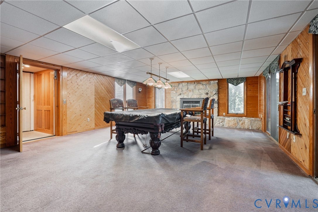 10862 Walton Lake Road, Dick Woods Subdivision, Disputanta, VA 23842 Interior space featuring diagonal wood-paneled walls, floor-to-ceiling stone fireplace surround, recessed ceiling lighting, three-light hanging fixture, and neutral carpeting
