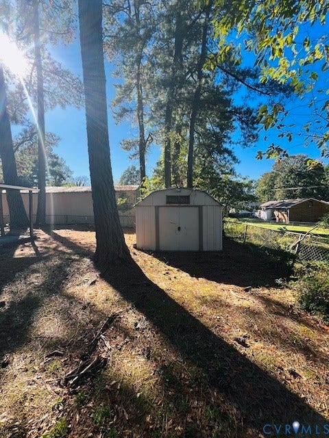 1525 Circle Drive, Petersburg, VA 23803 Exterior storage shed with a gambrel roof, metal siding, and double-door entry situated on a wooded lot featuring mature trees and chain-link perimeter fencing
