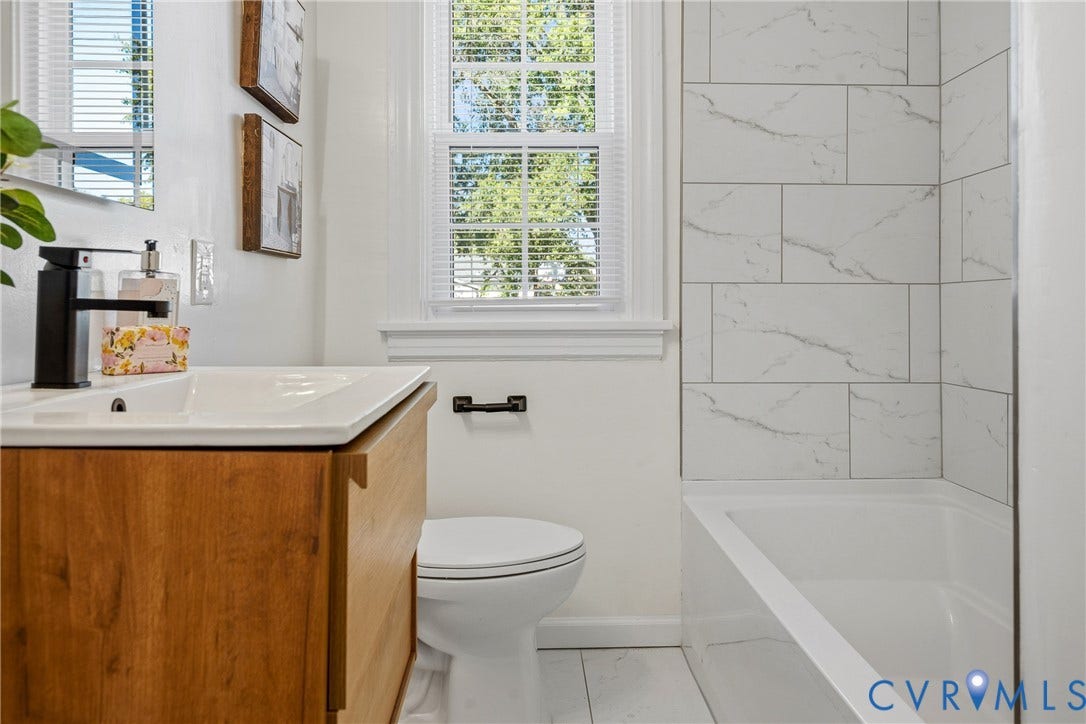 2106 Kenwood Avenue, Henrico, VA 22229 Bathroom featuring a wood-finish vanity with a white basin, matte black faucet, white tile shower surround with veining, and a window with a multi-pane sash