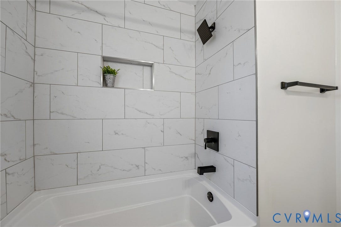 2106 Kenwood Avenue, Henrico, VA 22229 Bathtub surround featuring large-format white stone-pattern tile, a built-in recessed niche, matte black rainfall showerhead, matching matte black faucet, and a wall-mounted matte black towel bar