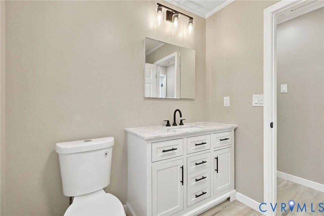 White shaker-style vanity with stone-top surface, undermount basin, matte black faucet, wall-mounted mirror, and three-light overhead fixture