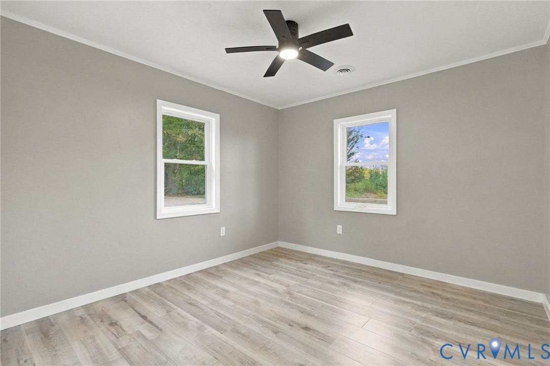 Neutral-toned interior featuring wood-finish flooring, two double-hung windows, and a central ceiling fan with an integrated light fixture