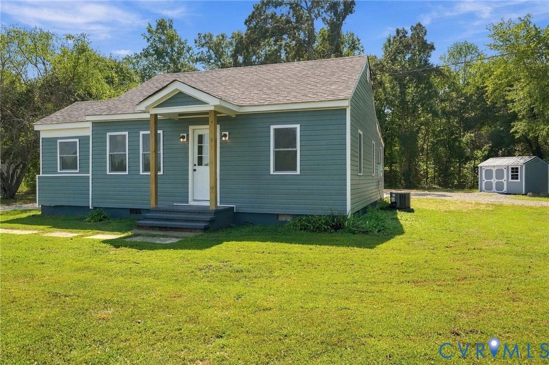 Single-story exterior featuring horizontal siding, a gabled roofline, a covered front entry with wooden support posts, and a detached storage structure