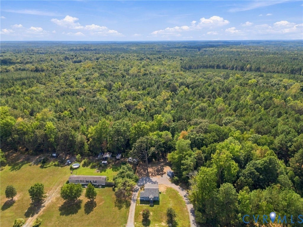 Aerial perspective of expansive acreage featuring mature woodland, cleared grass fields, and paved driveway access