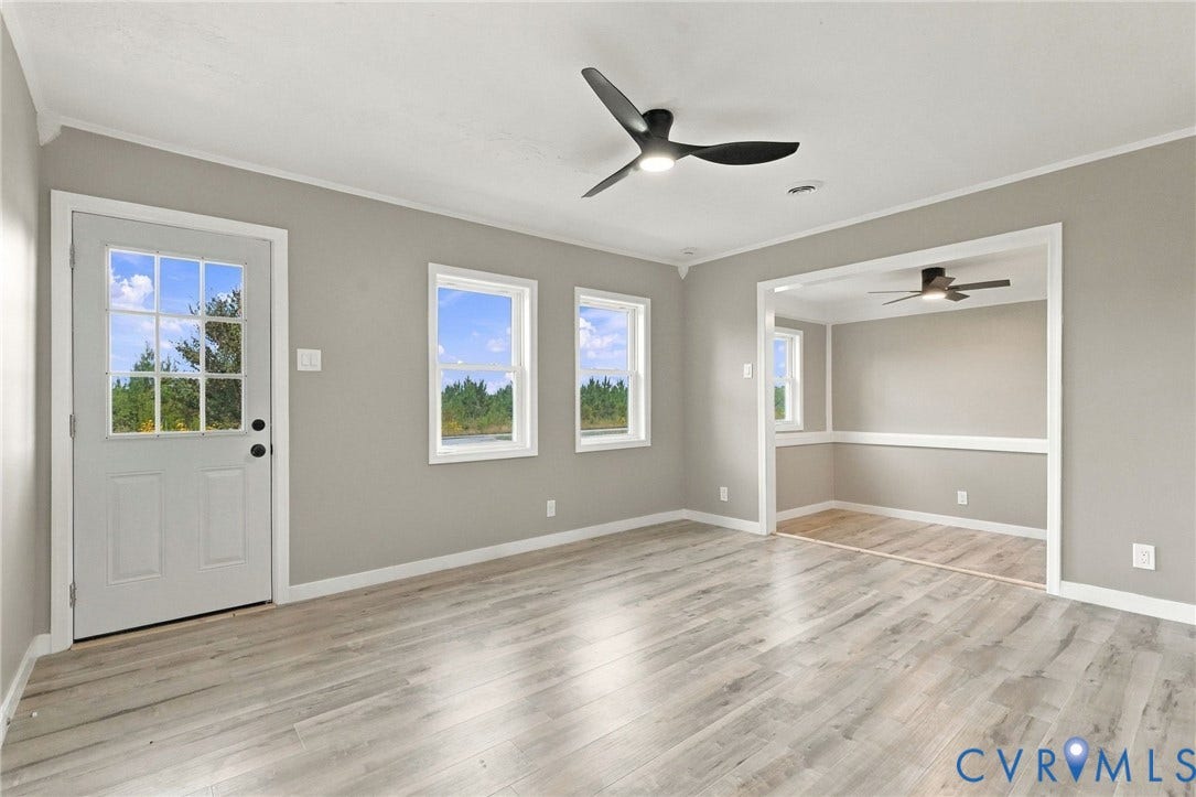 Neutral-toned walls, wood-finish flooring, multi-light glass panel door, matte black ceiling fans, and wainscoting detailing