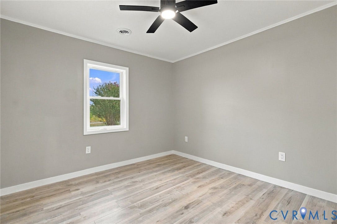 Neutral-toned interior featuring wood-finish flooring, a single-hung window, and a matte black ceiling fan with an integrated light fixture
