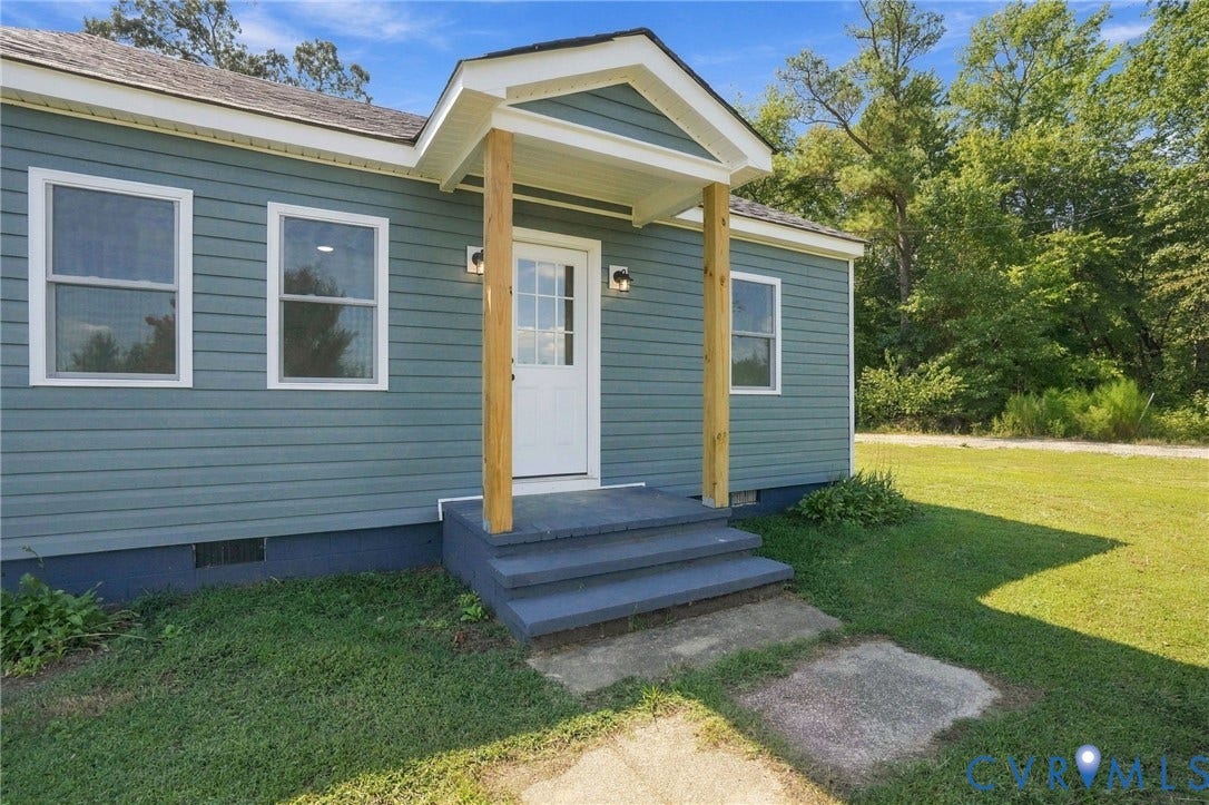 Exterior featuring blue horizontal siding, a covered entryway with wood-finish support columns, a gabled roofline, and concrete steps
