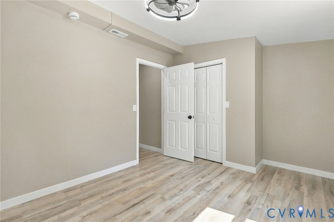 Neutral-toned interior featuring wood-finish flooring, a multi-panel door, bifold closet doors, and a ceiling-mounted light fixture