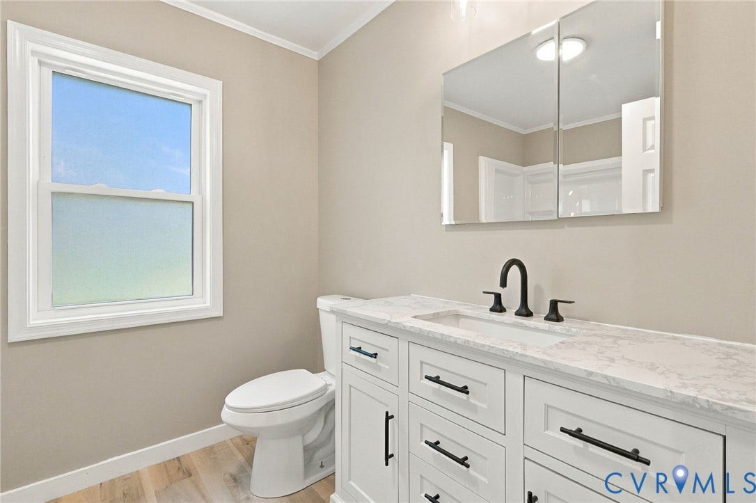 White vanity with stone-composite countertop, undermount sink, matte black faucet, and matching cabinet hardware, featuring wood-finish flooring and a dual-panel medicine cabinet