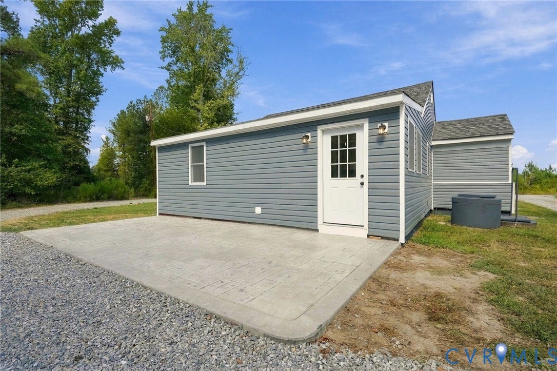 Exterior featuring blue horizontal siding, white trim, a textured concrete patio, and a multi-lite door with attached wall-mounted lighting