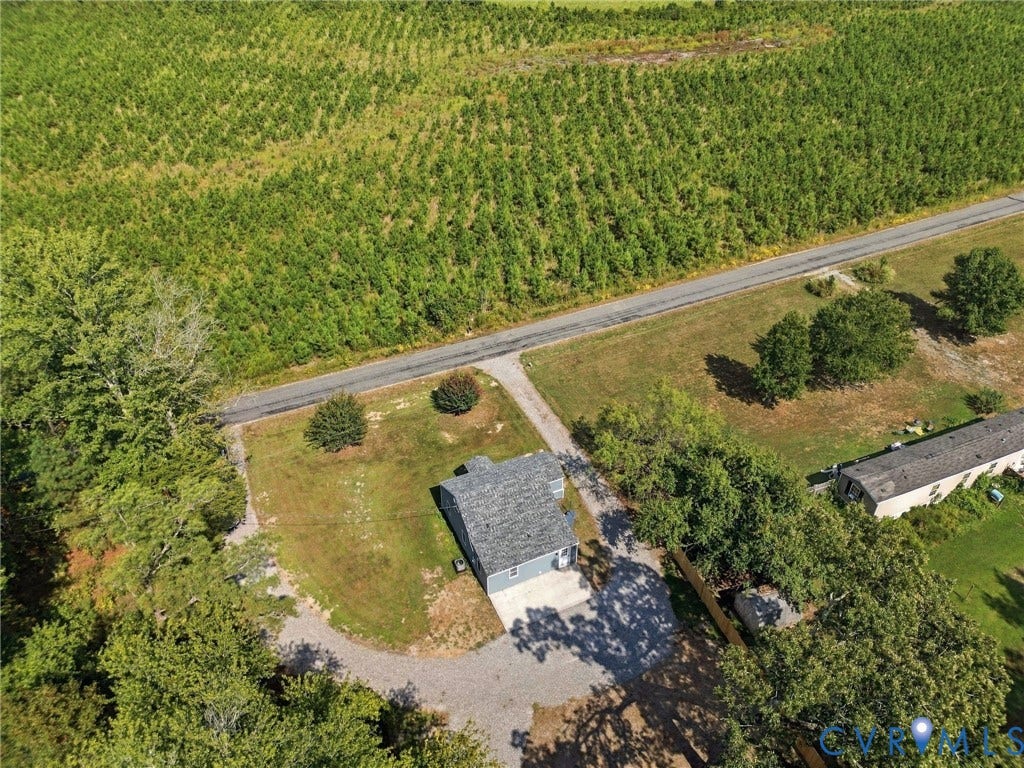 Aerial perspective of a property featuring a detached structure with a pitched roof, gravel driveway, mature trees, and expansive open space