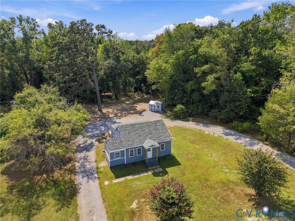 Single-story residence featuring a gray shingled roof, light blue siding, a graveled driveway, and an exterior storage structure situated on a partially wooded lot