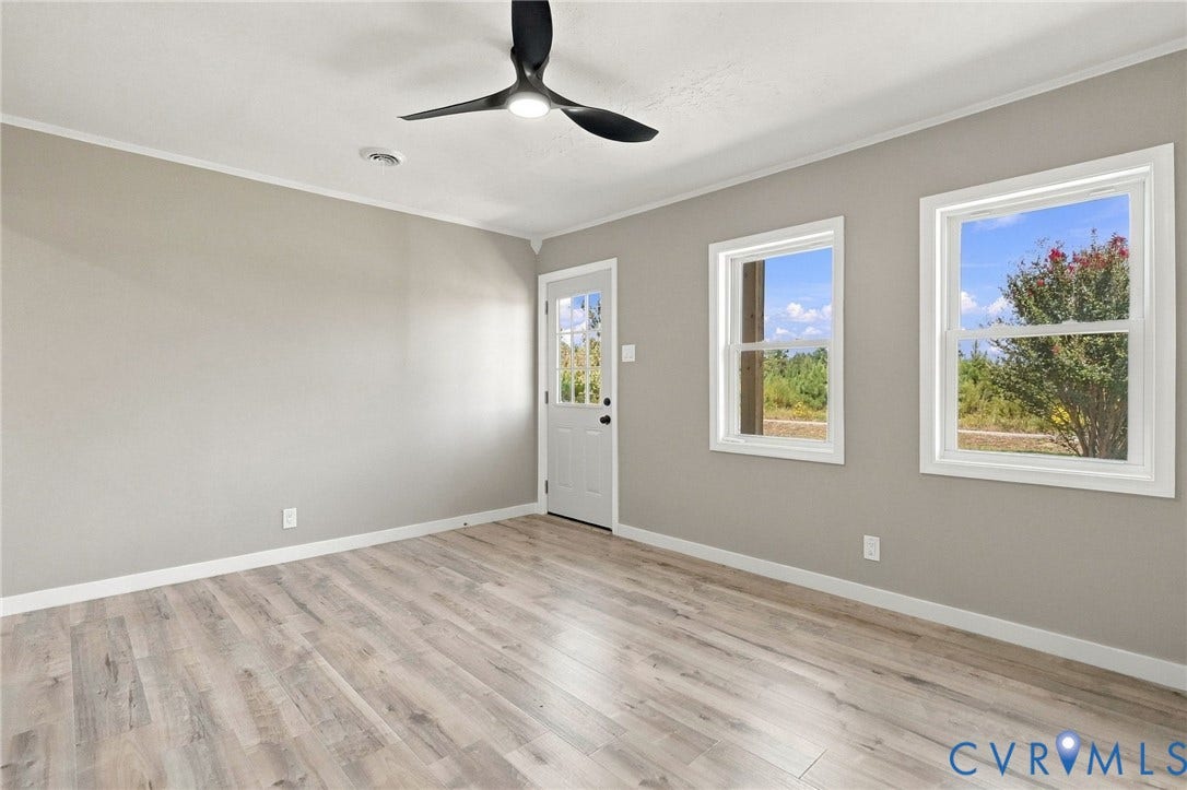 Neutral-toned interior space featuring wood-finish flooring, dual-pane windows, a contemporary matte black ceiling fan, and a glass-paneled exterior door