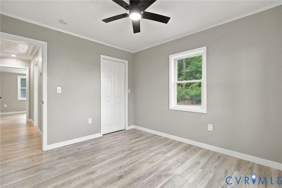 Neutral-toned interior space featuring light-colored wood-finish flooring, a ceiling fan with integrated lighting, and a single-panel interior door