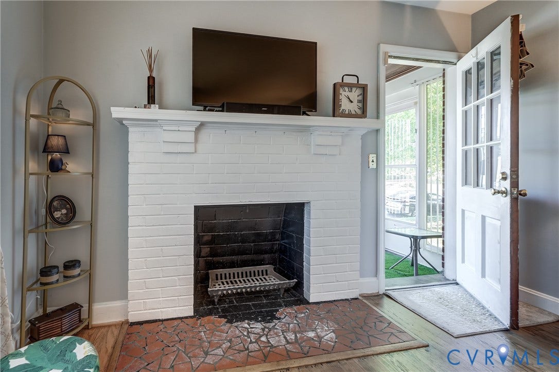 4007 Austin Avenue, Richmond, VA 23222 Painted white brick fireplace featuring a mantel shelf and a masonry hearth with a geometric tile inlay, wood-finish flooring, and a multi-pane glass entry door
