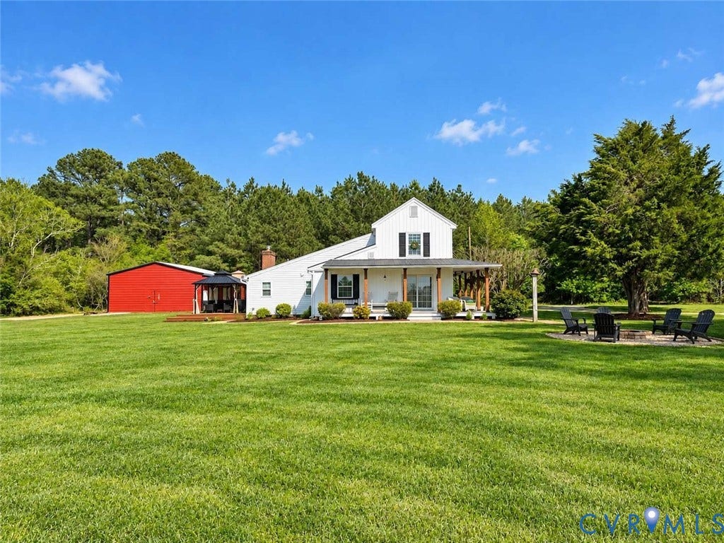 5424 Bellswood Drive, Mechanicsville, VA 23111 Expansive lawn featuring a white farmhouse with a covered front porch, a detached red metal barn, and a gravel fire pit area