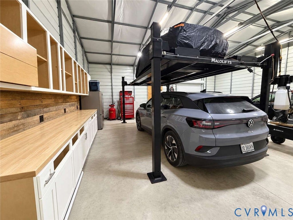 5424 Bellswood Drive, Mechanicsville, VA 23111 Workshop garage featuring high-clearance metal construction, integrated automotive lift, expansive wood-topped built-in cabinetry, and textured wood panel wall accents