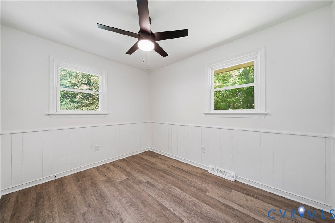 3622 New Bethel Road, Meherrin, VA 23954 Room featuring white wainscoting, wood-finish flooring, dual windows, and a dark-finish ceiling fan with an integrated light fixture