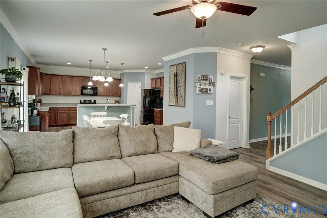 8909 Hollycroft Court, Mechanicsville, VA 23116 Open-concept kitchen featuring dark wood cabinetry, light-toned countertops, and a multi-light pendant fixture, complemented by wood-finish flooring and a staircase with a wooden handrail