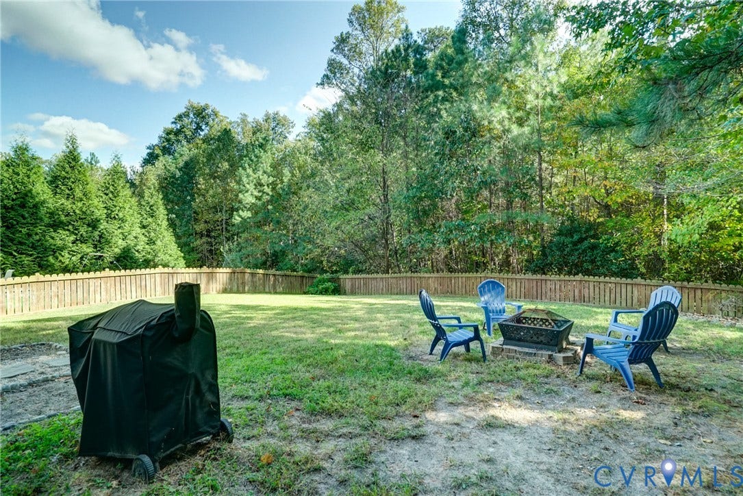 8909 Hollycroft Court, Mechanicsville, VA 23116 Expansive backyard featuring a wood-style perimeter fence, mature tree line, and stone-bordered fire pit area