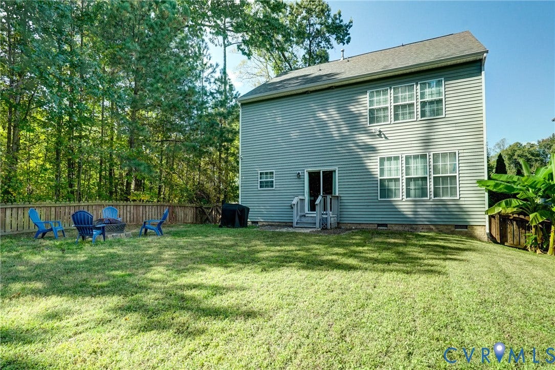 8909 Hollycroft Court, Mechanicsville, VA 23116 Two-story residence featuring light gray horizontal siding, an expansive rear lawn, perimeter wood fencing, a dedicated stone fire pit area, and a rear exterior staircase