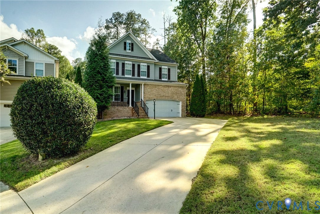 8909 Hollycroft Court, Mechanicsville, VA 23116 Two-story residence featuring a brick and horizontal siding exterior, a front-facing attached garage, a covered entryway with decorative railings, and a concrete driveway situated on a wooded lot