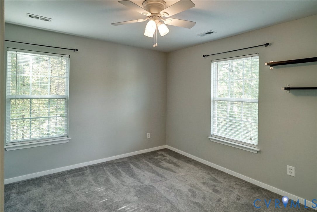 8909 Hollycroft Court, Mechanicsville, VA 23116 Neutral-toned interior room featuring wall-to-wall carpeting, dual windows with curtain rods, a ceiling fan with light fixture, and mounted wall shelving