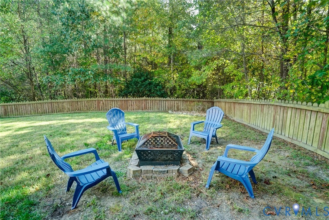 8909 Hollycroft Court, Mechanicsville, VA 23116 Backyard featuring a stone-lined fire pit, enclosed by a wood privacy fence and bordered by mature trees
