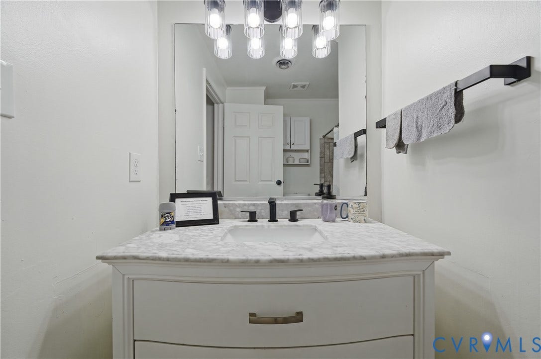 1101 Arch Hill Drive, Chesterfield, VA 23236 Vanity featuring a stone-top counter, undermount sink, matte black widespread faucet, large frameless mirror, and multi-bulb industrial-style light fixture