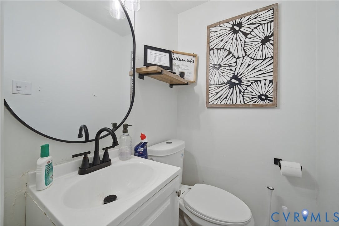 1101 Arch Hill Drive, Chesterfield, VA 23236 Round mirror with a black frame, white vanity with integrated basin, matte black faucet, and mounted wood-finish shelf