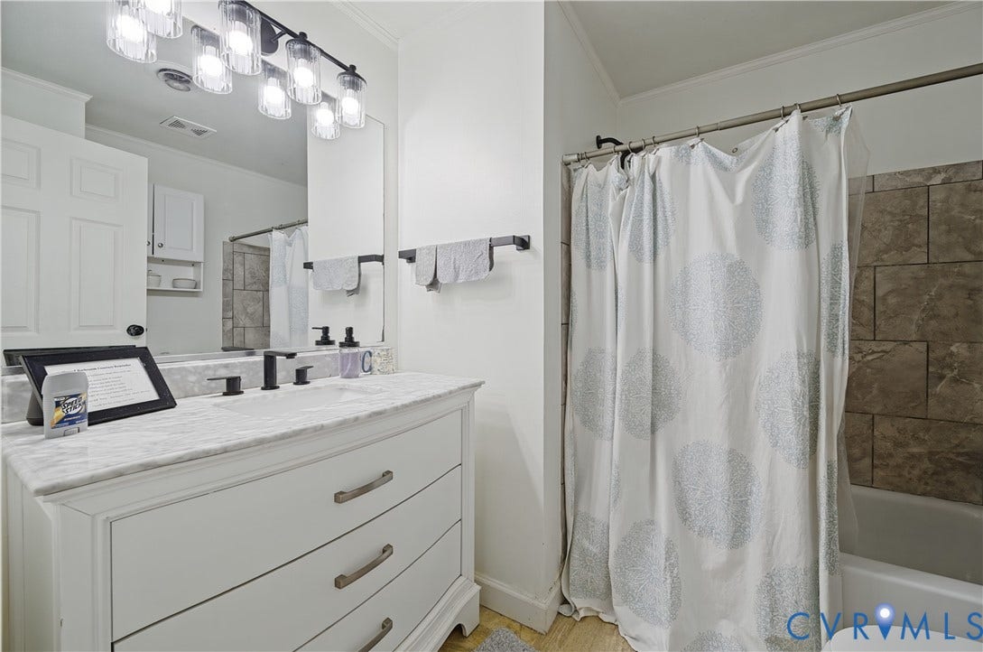 1101 Arch Hill Drive, Chesterfield, VA 23236 Bathroom vanity featuring a stone countertop, under-mount sink, matte black widespread faucet, multi-light vanity fixture, and large format tiled shower surround