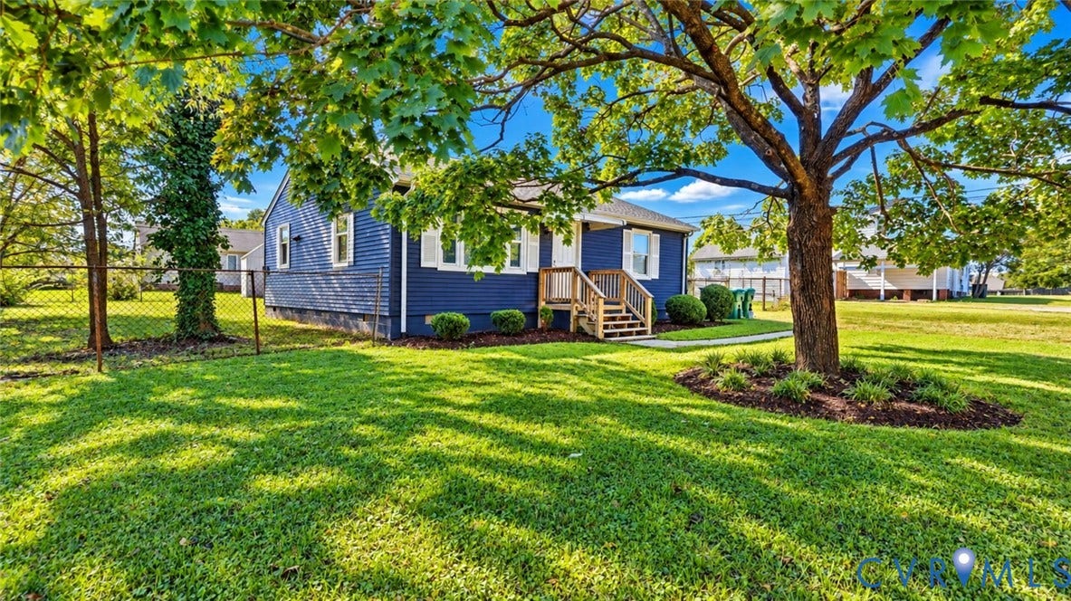 Blue-sided exterior featuring white shutters, a wood-constructed entry staircase, mature canopy trees, and an open lawn area