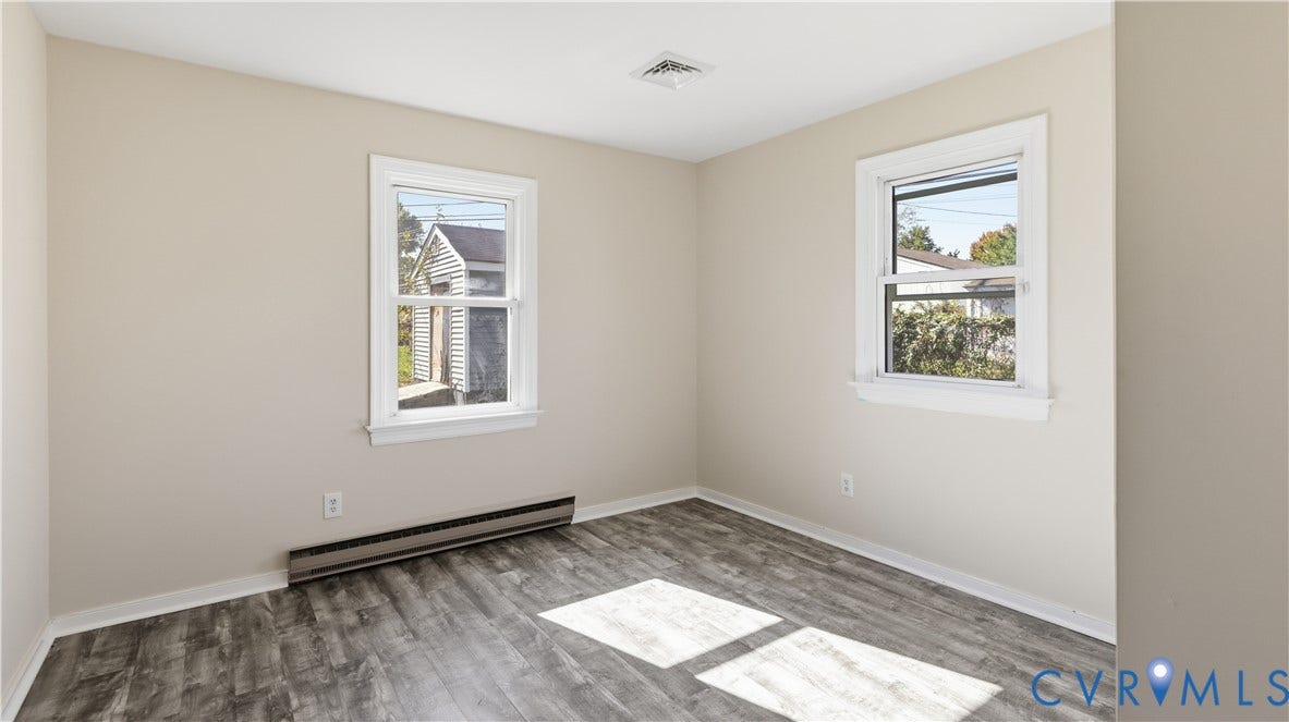 Interior room featuring wood-finish flooring, neutral-toned walls, and dual double-hung windows with white casing