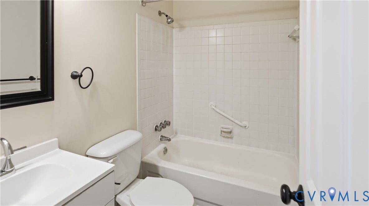 Bathroom featuring a white vanity with an integrated sink, a porcelain tub with a white tile surround, and black hardware finishes