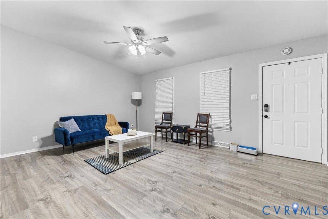 11518 Frederick Farms Circle, Midlothian, VA 23112 Neutral-toned interior space featuring wood-finish flooring, a multi-blade ceiling fan with integrated lighting, two windows with horizontal blinds, and a white six-panel entry door
