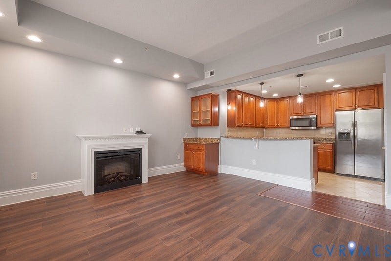 6 N 6th Street, #U3C, Downtown, Richmond, VA 23219 Living space featuring wood-finish flooring, a white mantel fireplace, recessed lighting, and a kitchen equipped with wooden cabinetry and a stone-surface breakfast bar