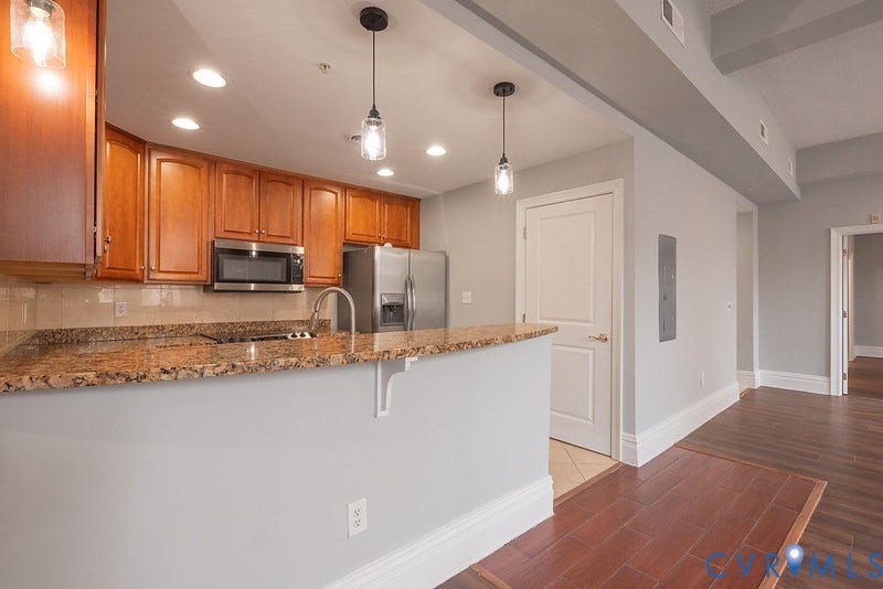 6 N 6th Street, #U3C, Downtown, Richmond, VA 23219 Kitchen featuring wood cabinetrhttps://studentaid.gov/fafsa-app/ROLESy, stone-surface breakfast bar, stainless steel appliances, pendant lighting, and wood-finish flooring