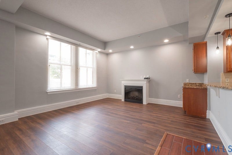 6 N 6th Street, #U3C, Downtown, Richmond, VA 23219 Living area featuring wood-finish flooring, a recessed ceiling with integrated lighting, a fireplace with a white mantel, and wood cabinetry with stone-finish countertops