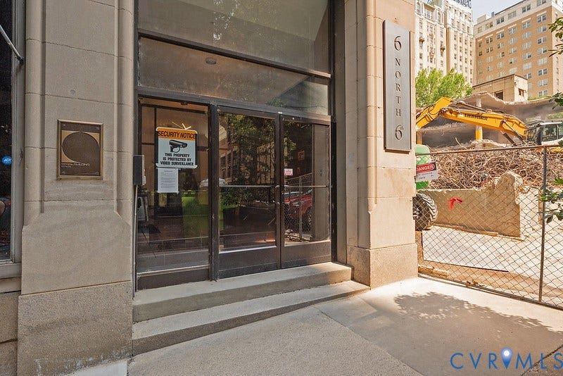 6 N 6th Street, #U3C, Downtown, Richmond, VA 23219 Stone-clad building facade featuring a glass entry door, multi-pane transom window, and prominent metallic building signage